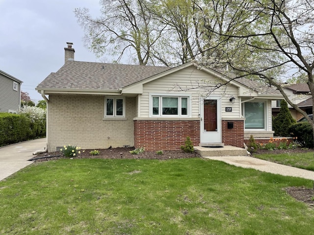 view of front of property featuring roof with shingles, a chimney, a front yard, and brick siding