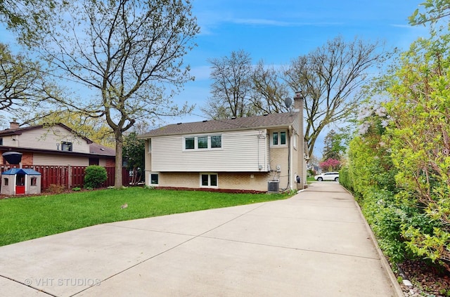 rear view of house with driveway, a chimney, a lawn, brick siding, and cooling unit