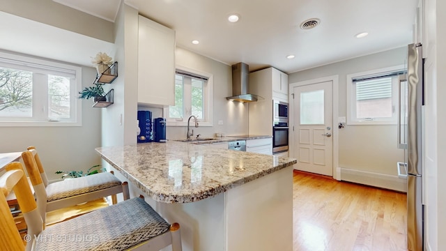 kitchen featuring wall chimney range hood, visible vents, appliances with stainless steel finishes, a sink, and a peninsula