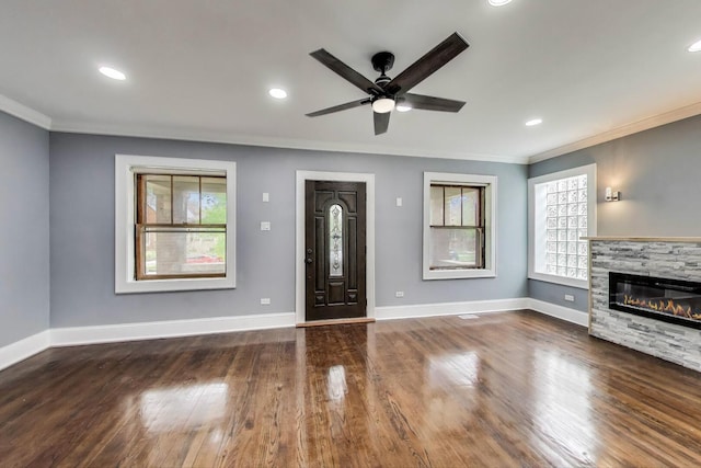 unfurnished living room featuring plenty of natural light, crown molding, ceiling fan, a fireplace, and wood finished floors