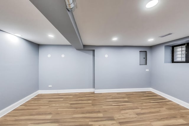 finished basement with light wood-type flooring, baseboards, electric panel, and recessed lighting