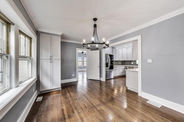 unfurnished dining area featuring a chandelier, dark wood-type flooring, baseboards, and crown molding