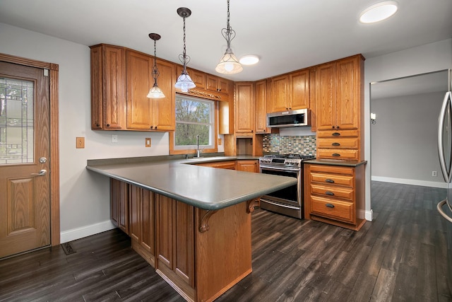 kitchen with appliances with stainless steel finishes, a sink, brown cabinetry, baseboards, and dark wood-type flooring