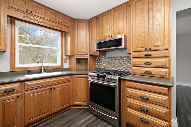 kitchen with dark countertops, tasteful backsplash, a sink, stainless steel appliances, and dark wood-type flooring