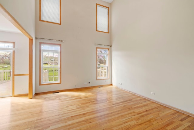 unfurnished living room featuring plenty of natural light, light wood finished floors, and a high ceiling