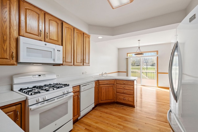 kitchen with light countertops, a sink, a peninsula, light wood-style floors, and white appliances