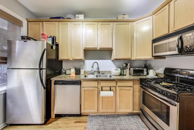 kitchen featuring light brown cabinetry, a sink, stainless steel appliances, and light wood-type flooring