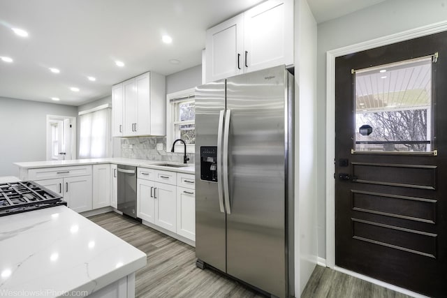 kitchen featuring white cabinetry, light stone countertops, appliances with stainless steel finishes, and a sink