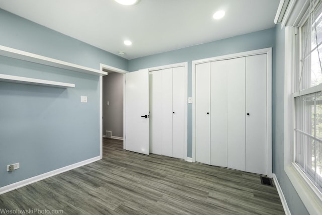 unfurnished bedroom featuring baseboards, two closets, visible vents, and wood finished floors