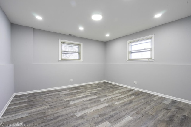 below grade area with a healthy amount of sunlight, baseboards, wood finished floors, and visible vents
