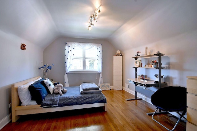 bedroom with wood finished floors, vaulted ceiling, baseboards, and rail lighting
