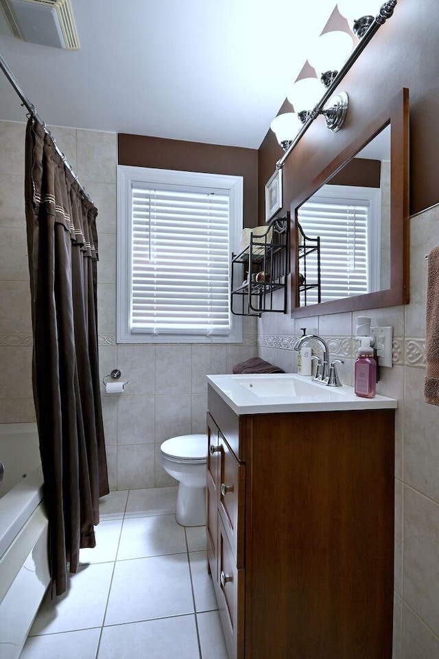 full bath with tile walls, toilet, vanity, tile patterned floors, and shower / bath combo
