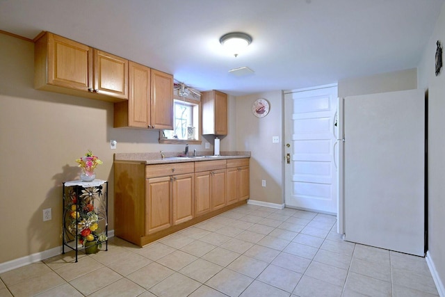 kitchen with freestanding refrigerator, light countertops, a sink, light tile patterned floors, and baseboards