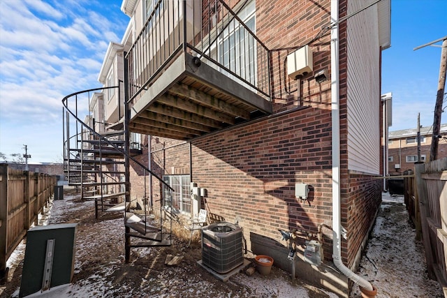 view of property exterior featuring fence, central AC unit, stairs, and brick siding