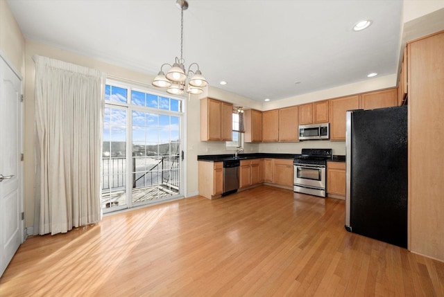kitchen with a sink, a notable chandelier, light wood-style flooring, dark countertops, and appliances with stainless steel finishes