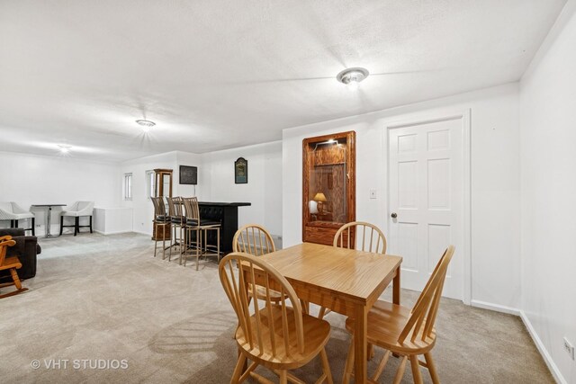 dining room featuring baseboards, light colored carpet, and a bar