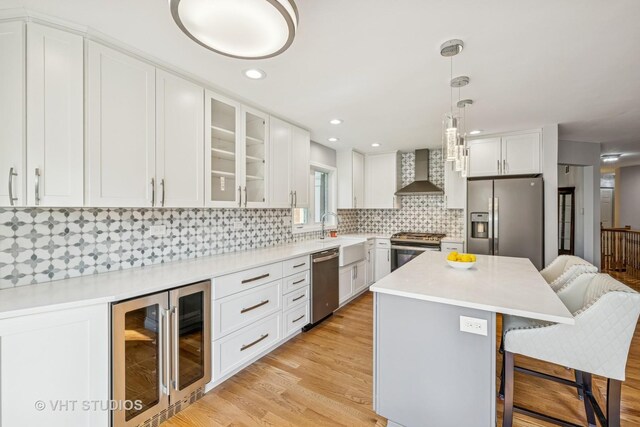 kitchen featuring wine cooler, a kitchen breakfast bar, wall chimney range hood, a sink, and appliances with stainless steel finishes