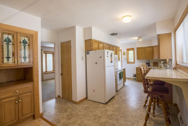 kitchen with brown cabinets, light countertops, baseboards, white appliances, and backsplash