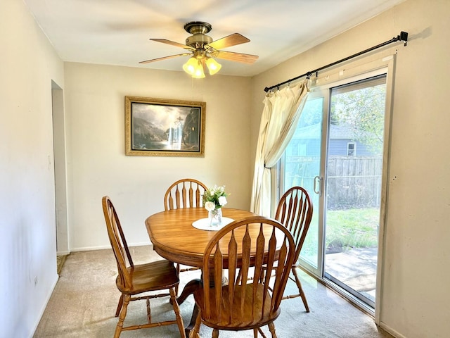 dining room featuring light colored carpet, a ceiling fan, and baseboards