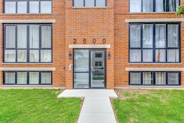 entrance to property featuring brick siding, french doors, and a lawn