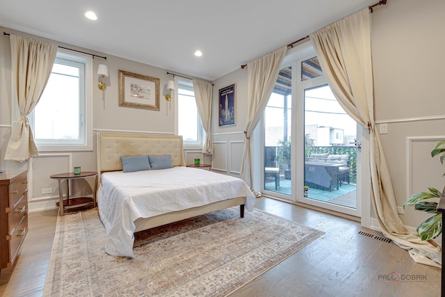 bedroom featuring light wood finished floors, access to outside, a wainscoted wall, visible vents, and a decorative wall