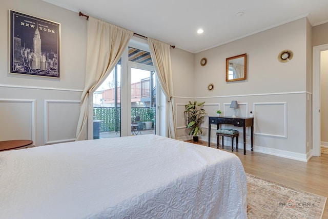 bedroom with access to exterior, wood finished floors, ornamental molding, and a decorative wall