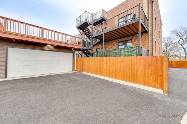 view of home's exterior with driveway, a balcony, fence, brick siding, and a garage