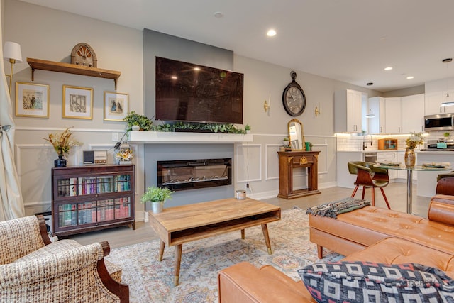living area featuring recessed lighting, a decorative wall, wainscoting, a glass covered fireplace, and light wood-type flooring