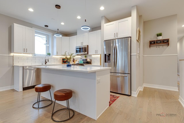 kitchen featuring white cabinetry, a breakfast bar, stainless steel appliances, a kitchen island, and backsplash