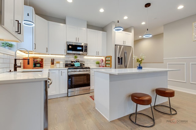 kitchen featuring a sink, stainless steel appliances, a center island, light wood-style flooring, and white cabinets