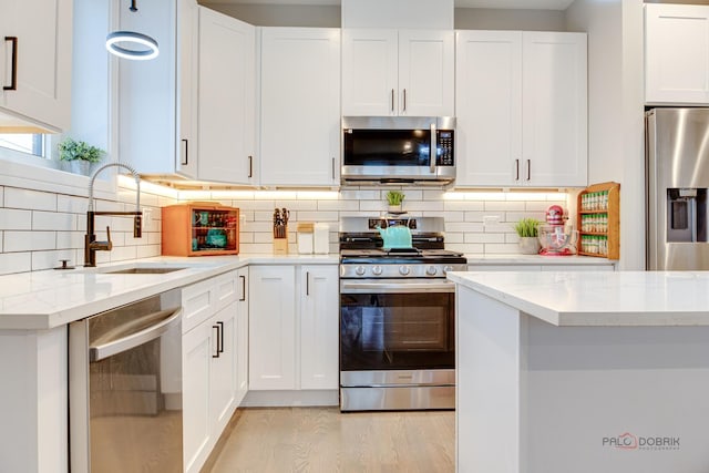 kitchen with light wood finished floors, light stone countertops, a sink, stainless steel appliances, and white cabinetry