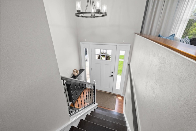 foyer entrance with stairs, a textured wall, an inviting chandelier, and wood finished floors