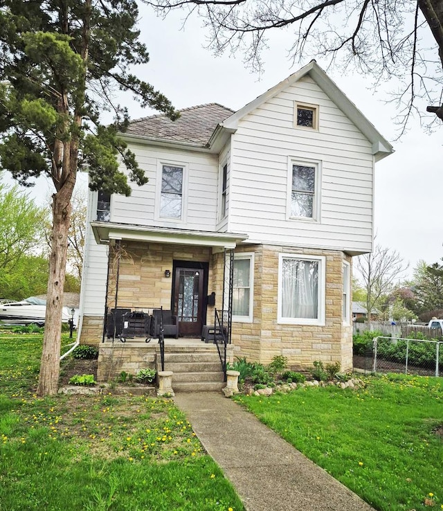 traditional-style house with fence, covered porch, a front lawn, and stone siding