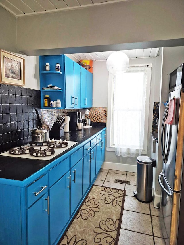 kitchen with dark countertops, stovetop, freestanding refrigerator, and blue cabinetry