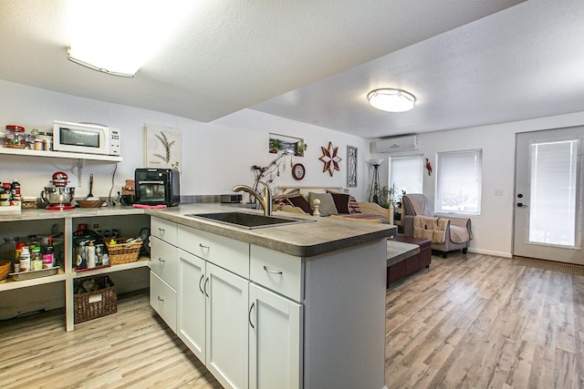 kitchen featuring a sink, a peninsula, open floor plan, light wood-type flooring, and white microwave