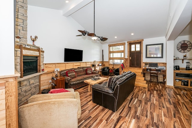 living area with a ceiling fan, a stone fireplace, beam ceiling, wood finished floors, and recessed lighting