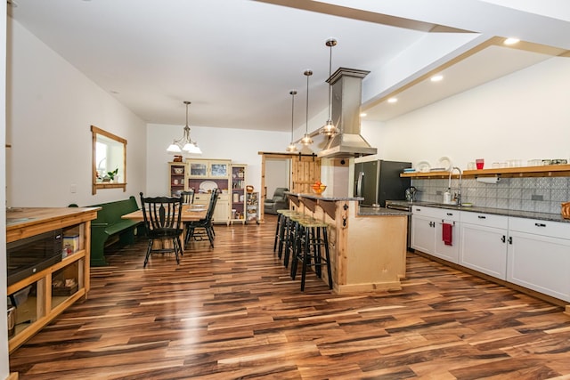 kitchen with a breakfast bar area, stainless steel refrigerator with ice dispenser, dark wood-type flooring, a center island, and tasteful backsplash