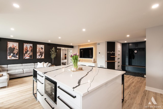 kitchen featuring black microwave, open floor plan, a kitchen breakfast bar, a spacious island, and light wood-style flooring