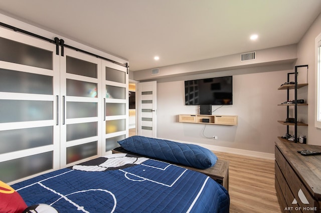bedroom featuring baseboards, visible vents, a barn door, and wood finished floors