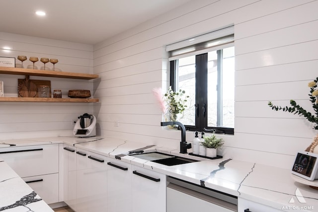 kitchen with light stone countertops, open shelves, wood walls, a sink, and white cabinetry