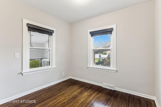 empty room with visible vents, baseboards, dark wood-style flooring, and a healthy amount of sunlight