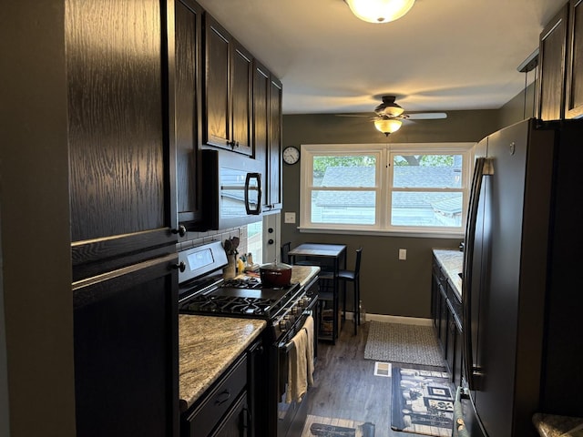 kitchen featuring freestanding refrigerator, gas range, ceiling fan, dark wood-style flooring, and baseboards