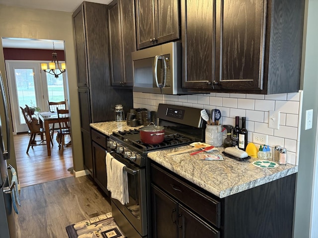 kitchen with decorative backsplash, stainless steel appliances, dark brown cabinetry, wood finished floors, and a notable chandelier