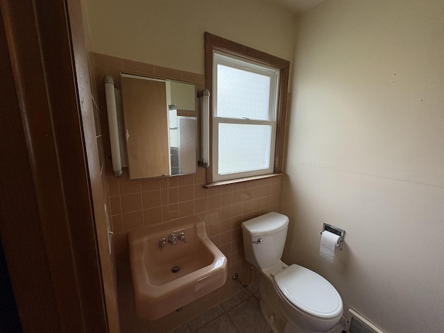 half bath featuring tile patterned floors, toilet, tile walls, and a sink