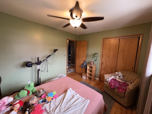 bedroom featuring wood finished floors, a closet, baseboards, visible vents, and a ceiling fan