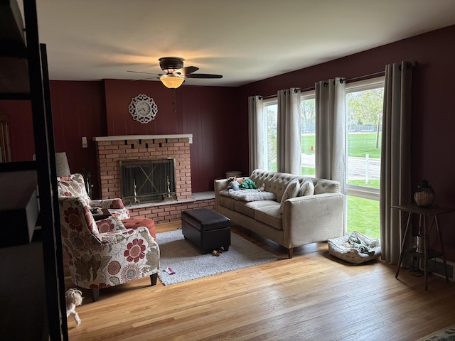 living room with wood finished floors, a ceiling fan, and a brick fireplace