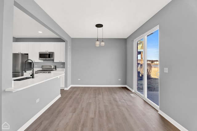 unfurnished dining area with a sink, light wood-style floors, recessed lighting, and baseboards