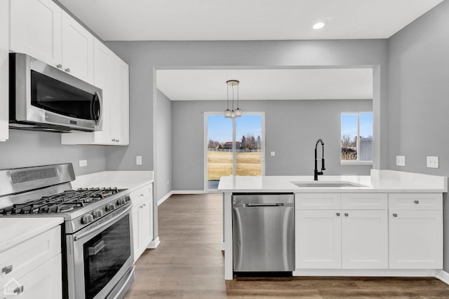 kitchen featuring a sink, stainless steel appliances, a peninsula, light countertops, and white cabinets