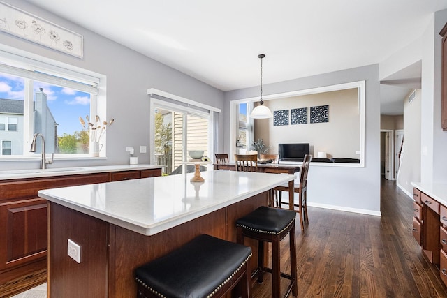 kitchen featuring pendant lighting, dark wood finished floors, a sink, light countertops, and a breakfast bar