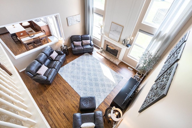 living room with a towering ceiling, a glass covered fireplace, and wood finished floors